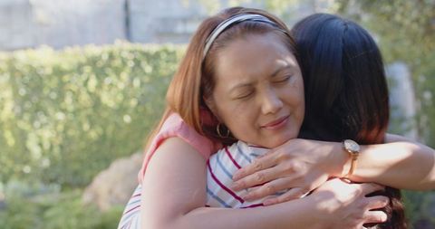 Asian Mother and Daughter Hugging in Sunlit Backyard