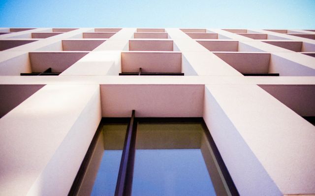 Modern building facade with repetitive architectural patterns seen from a low-angle perspective. Ideal for use in architectural portfolios, urban development projects, and promotional materials for real estate companies. The image showcases the beauty of minimalist and contemporary design with its clean lines and geometric shapes.