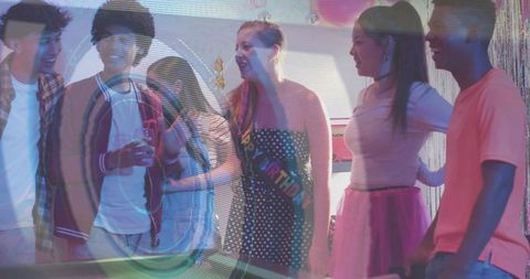 Birthday friends laughing around pool table with polka-dot sash and colorful party lights