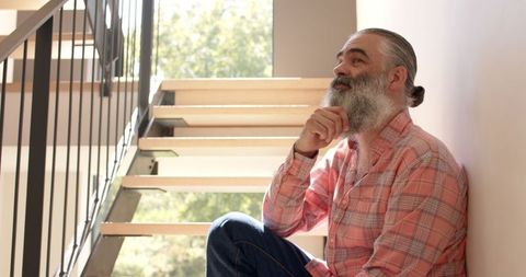 Senior man in plaid shirt sitting on stairs in deep thought