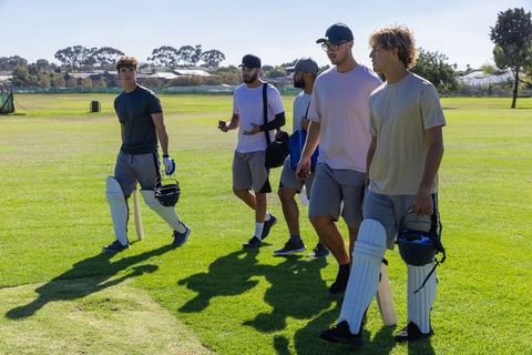 Young cricket players walking off field after training carrying bats, pads, helmets
