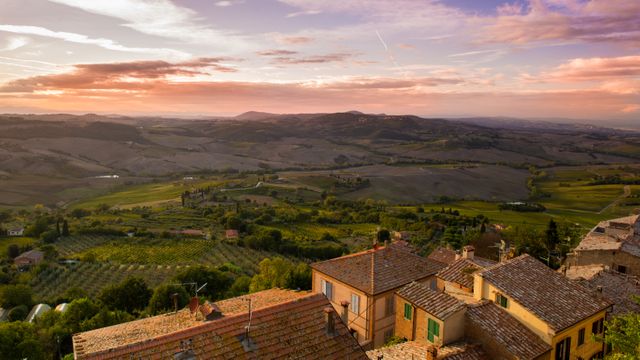 View of rolling hills and valleys during sunset with rooftops in foreground; scenic landscape with illuminating evening light. Well-suited for travel, nature, and landscape themes; ideal for use in tourism promotions, environmental articles, or as illustrative content for rural or countryside features.