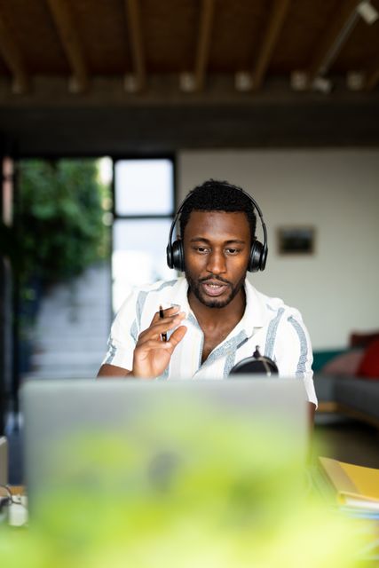 Vertical image of african american man in headphones making laptop video call at home, copy space. Working from home, communication, inclusivity and lifestyle.