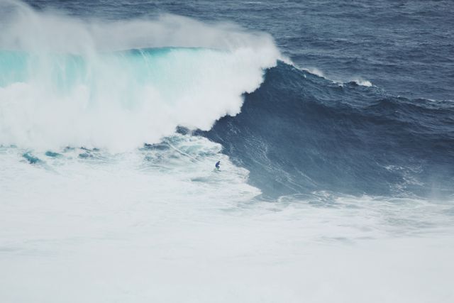 A surfer braves a massive ocean wave, showcasing determination and skill. Ideal for content related to extreme sports, adventure, and the power of nature. Suitable for use in magazines, advertisements, and articles promoting surfing, beaches, or ocean conservation.