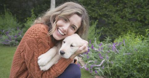 Woman Joyfully Cuddling Golden Retriever Puppy on Green Lawn