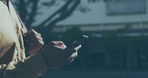 Person Checking Smartphone on City Sidewalk in Mustard Shirt