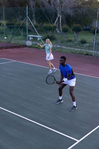 Mixed doubles tennis partners playing on outdoor fenced court practicing teamwork and focus