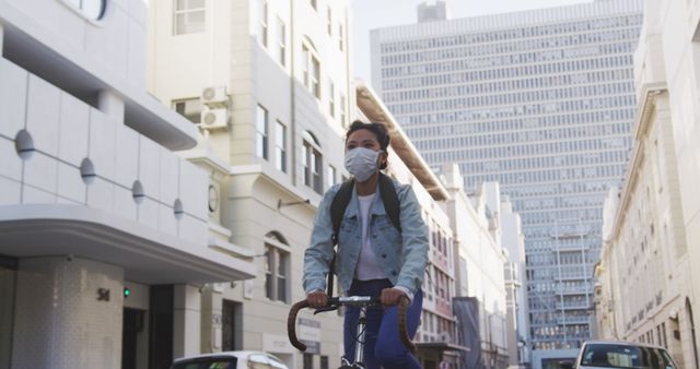 This image depicts a young woman cycling through an urban environment while wearing a face mask and carrying a backpack. Perfect for illustrating topics related to urban commuting, public health measures, eco-friendly transportation, and city life. Suitable for use in articles, blogs, and campaigns promoting healthy, safe commuting options.
