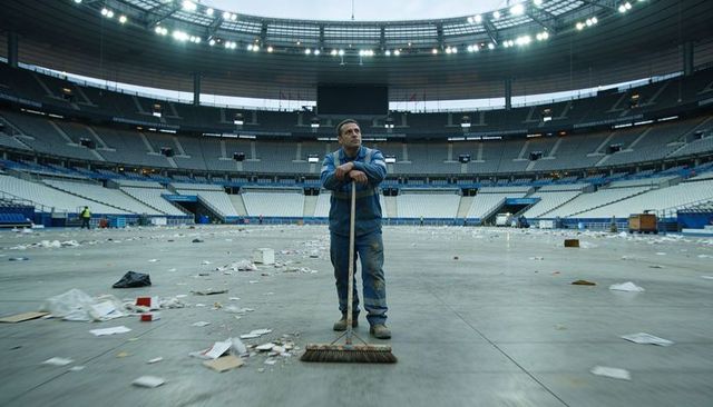 Stadium cleaner sweeping debris across empty arena floor after crowd exit