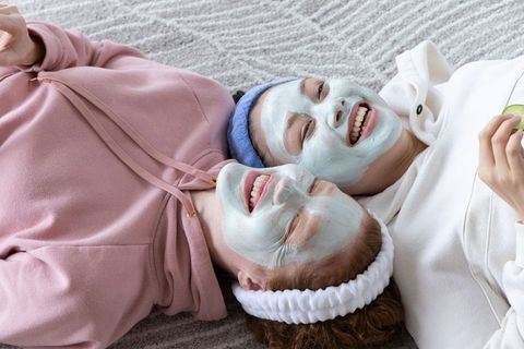 Friends enjoying at-home spa night wearing facial masks and relaxing with cucumbers