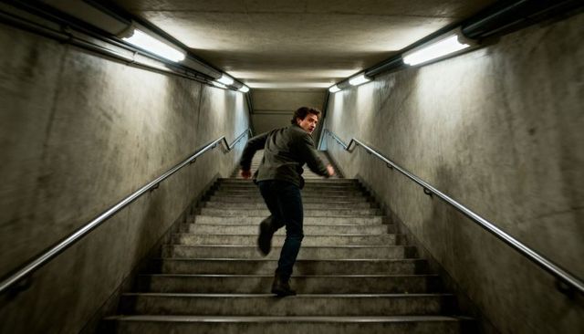 Man running up concrete staircase in underpass turning back under fluorescent lighting