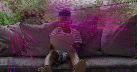 African american boy sitting on couch using tablet with magenta digital light trails