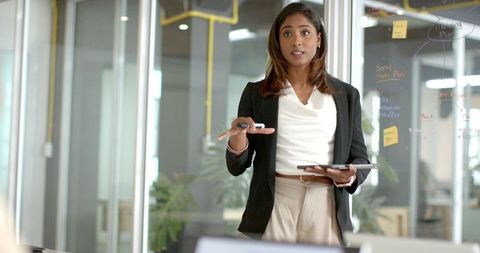 Indian businesswoman presenting strategy with tablet and marker in modern glass meeting room