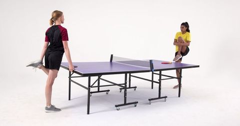 Female Athletes Stretching by Ping Pong Table Preparing for Game