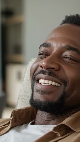 Reclining Black man smiling and laughing while relaxing at home vertical video