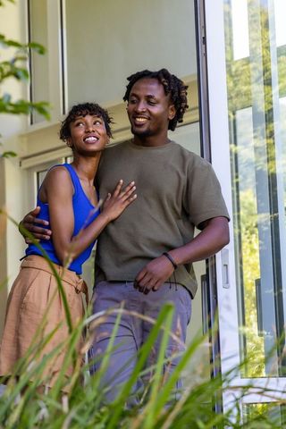 African american couple leaning in modern doorway enjoying sunlight and green home moment