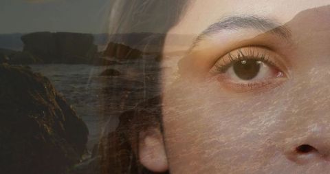 Dreamlike double exposure portrait blending female eye with rocky shoreline and sunset waves