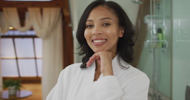 Portrait of biracial woman wearing bathrobe looking at camera and smiling. domestic life, spending quality free time relaxing at home.