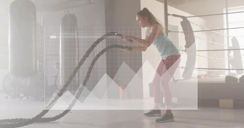 Woman swinging battle ropes in gym with performance graph overlay for fitness training