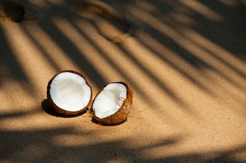 Cracked coconut halves lying on sunlit tropical sand with palm shadow and footprints