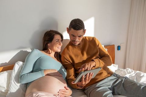 Expecting Couple Using Tablet in Bed Celebrating Pregnancy