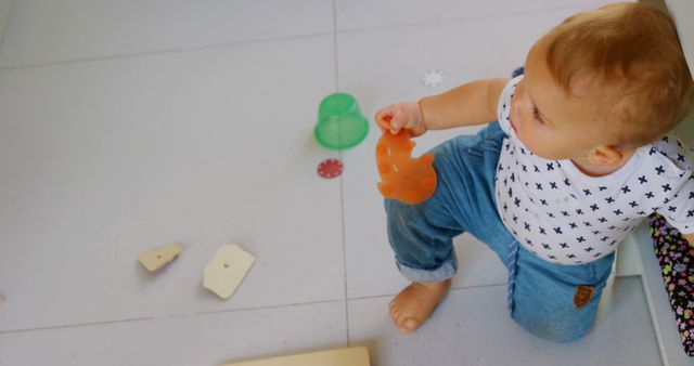 Happy caucasian toddler boy in jeans playing with toys in kitchen, copy space. Childhood, learning, play, discovery and domestic life, unaltered.