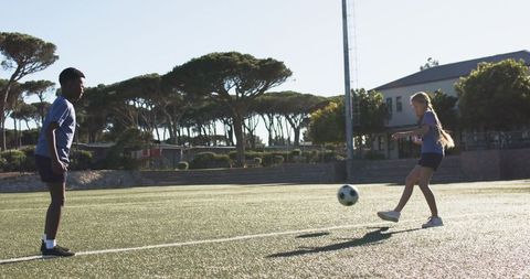 Backlit teenagers practicing soccer passing on artificial turf with dynamic long shadows