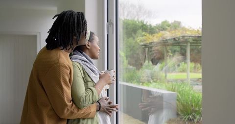 African American couple embracing by glass door enjoying coffee and garden view