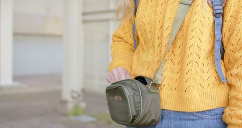 Woman wearing mustard knit sweater holding olive crossbody bag on urban street