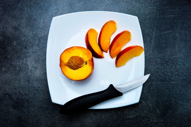 Image showcasing sliced peach and a knife on a white plate. Ideal for food blogs, recipe websites, cooking magazines, and nutrition guides. Represents freshness and healthy eating.