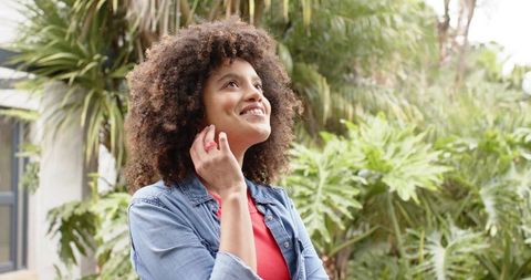 Young african american woman gazing upward in tropical backyard wearing denim jacket