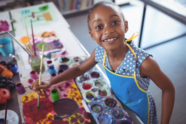 Young girl enjoying painting activity in classroom, showcasing creativity and artistic expression. Ideal for educational content, school brochures, art class promotions, and articles on childhood development and creativity.