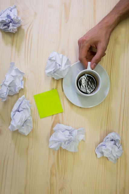 Hand of man holding cup of coffee with crumpled paper on a desk