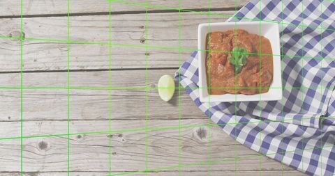 Square bowl of tomato dip garnished with cilantro on gingham cloth over rustic wood planks