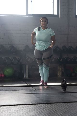 African american woman preparing for barbell lift in gym wearing teal fitness outfit