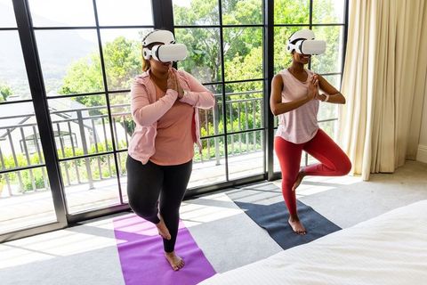 African american women practicing vr yoga balancing on mats in sunny bedroom