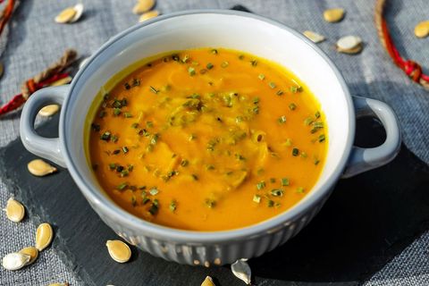 Creamy Roasted Pumpkin Soup Garnishing with Chives in Gray Ceramic Bowl on Slate