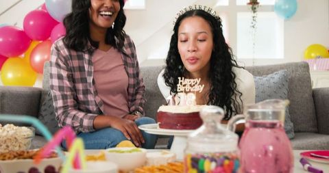 Young women celebrating birthday with cake and colorful balloons at home