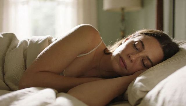 Sunlit middle-aged woman sleeping peacefully on side in cozy neutral bedroom with soft duvet