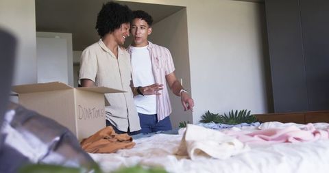 Two men packing donations in bedroom sorting clothing for charity and home organizing