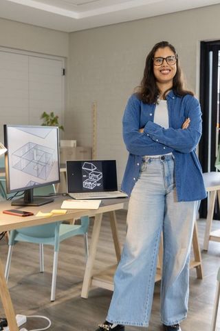 Asian woman architect standing with arms crossed in modern studio showing 3d cad designs