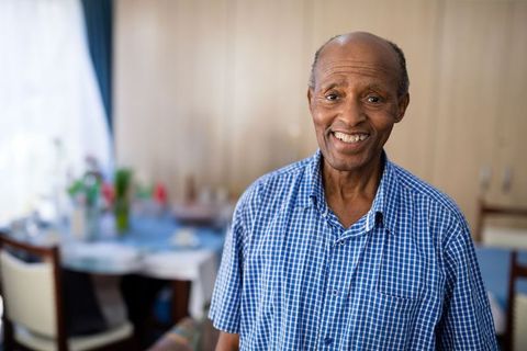 Smiling senior man in blue plaid shirt by dining room table with flowers