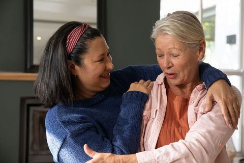 Mature women embracing and smiling together in cozy home, sharing warm intergenerational hug