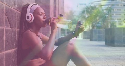 Fitness break: woman resting after run drinking water wearing headphones and smartwatch