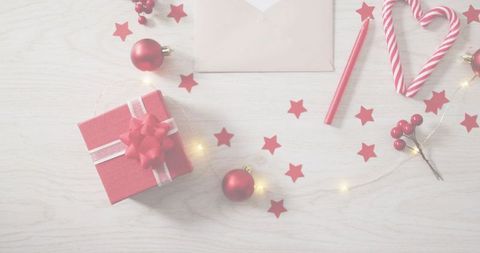 Festive flatlay featuring red gift box, candy cane heart, envelope, baubles and twinkle lights