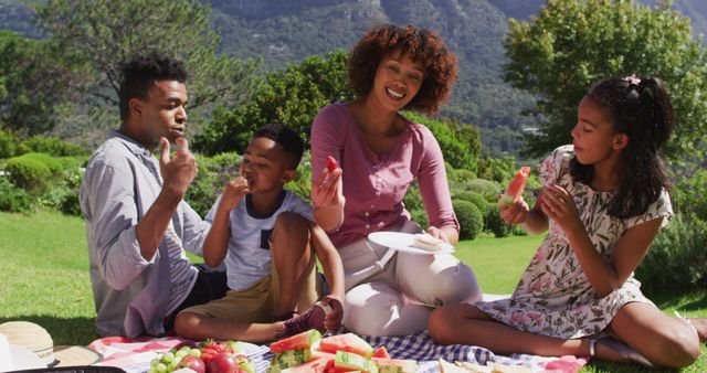 Happy african american parents, daughter and son sitting outdoors on blanket, eating fruits. staying in garden in isolation during quarantine lockdown