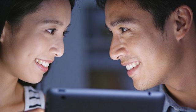 Smiling couple leaning close watching tablet screen at home cozy intimate evening