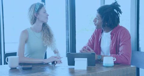 Young colleagues discussing project over tablet at sunlit cafe workspace