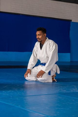 Martial artist kneeling in gi with blue belt demonstrating focus
