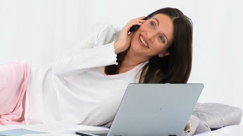Smiling Woman Talking on Phone with Laptop in Bedroom